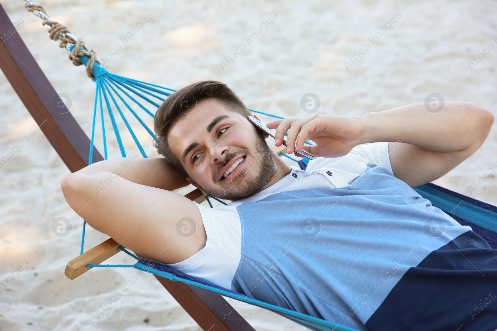 Photo of Young man talking on phone in hammock at seaside