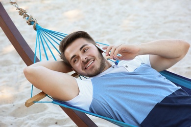 Photo of Young man talking on phone in hammock at seaside