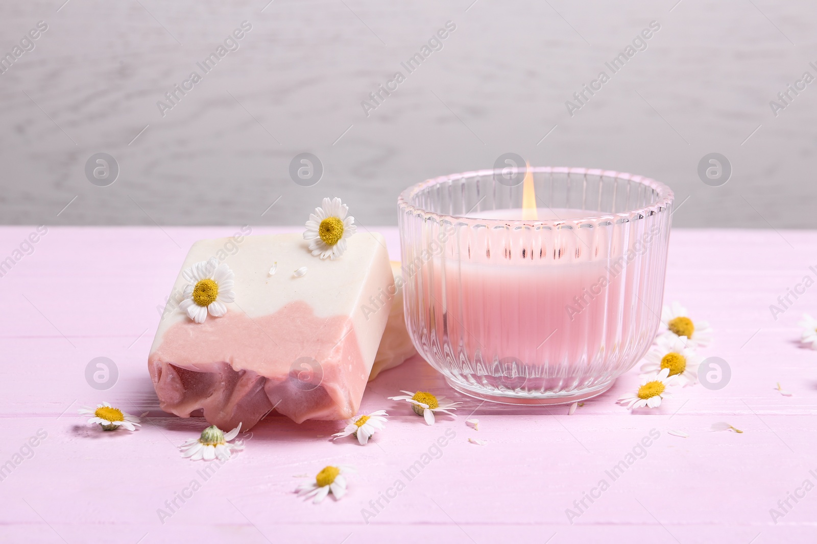 Photo of Chamomile flowers, soap bars and burning candle on pink wooden table