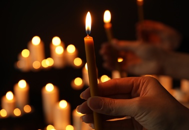 Photo of Woman holding burning candle in darkness against blurred background, closeup
