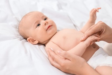 Woman applying body cream onto baby`s skin on bed, closeup