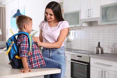 Happy mother and little child with backpack ready for school in kitchen