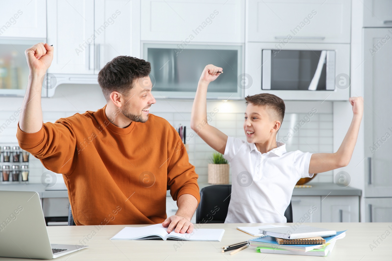 Photo of Happy dad and son after finishing homework in kitchen