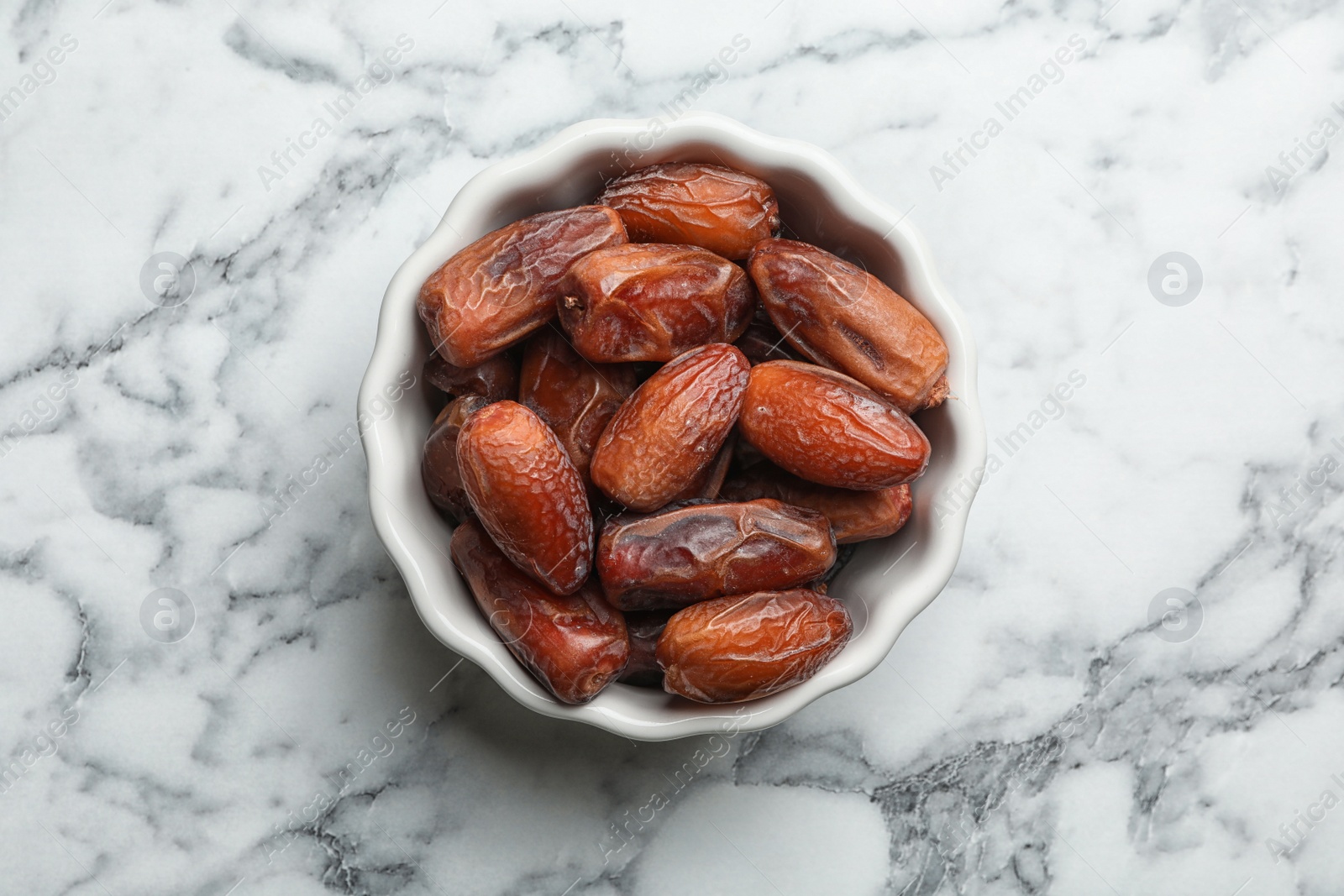 Photo of Bowl with sweet dried date fruits on marble background, top view