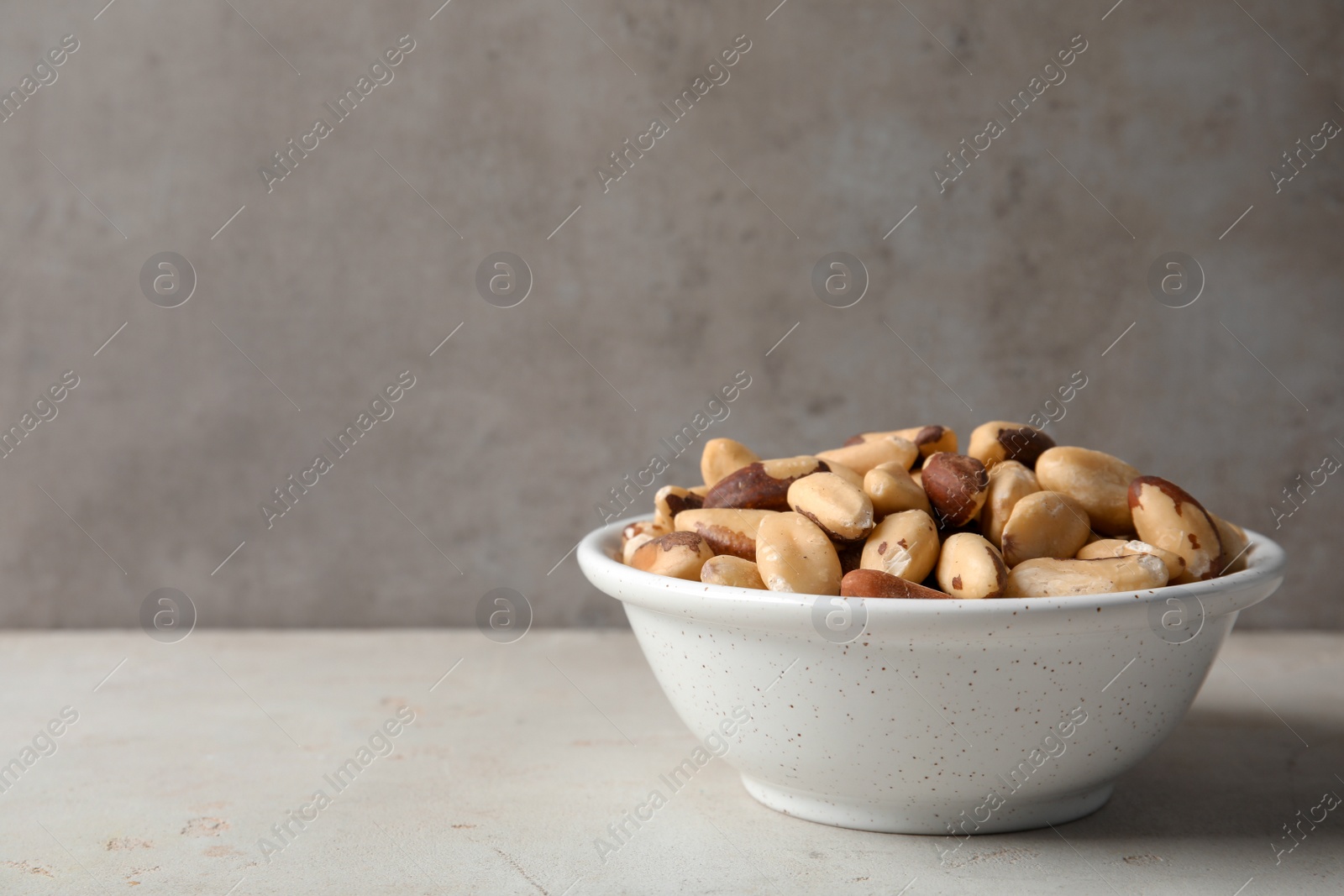 Photo of Bowl with tasty Brazil nuts on grey table. Space for text
