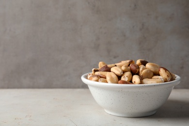 Photo of Bowl with tasty Brazil nuts on grey table. Space for text