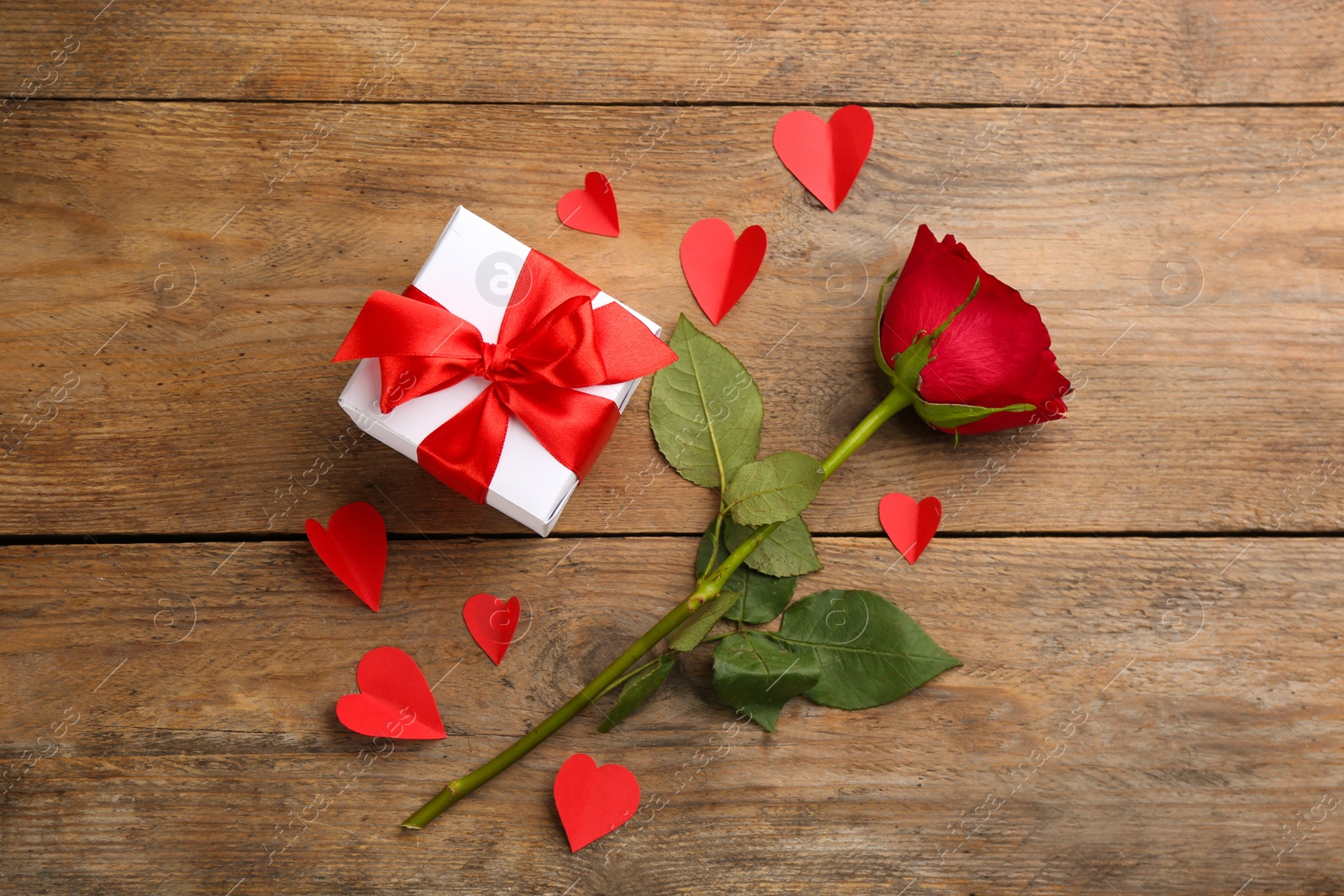 Photo of Beautiful gift box, paper hearts and rose on wooden table, flat lay. Valentine's Day celebration