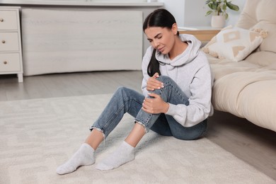 Photo of Woman suffering from knee pain near sofa at home