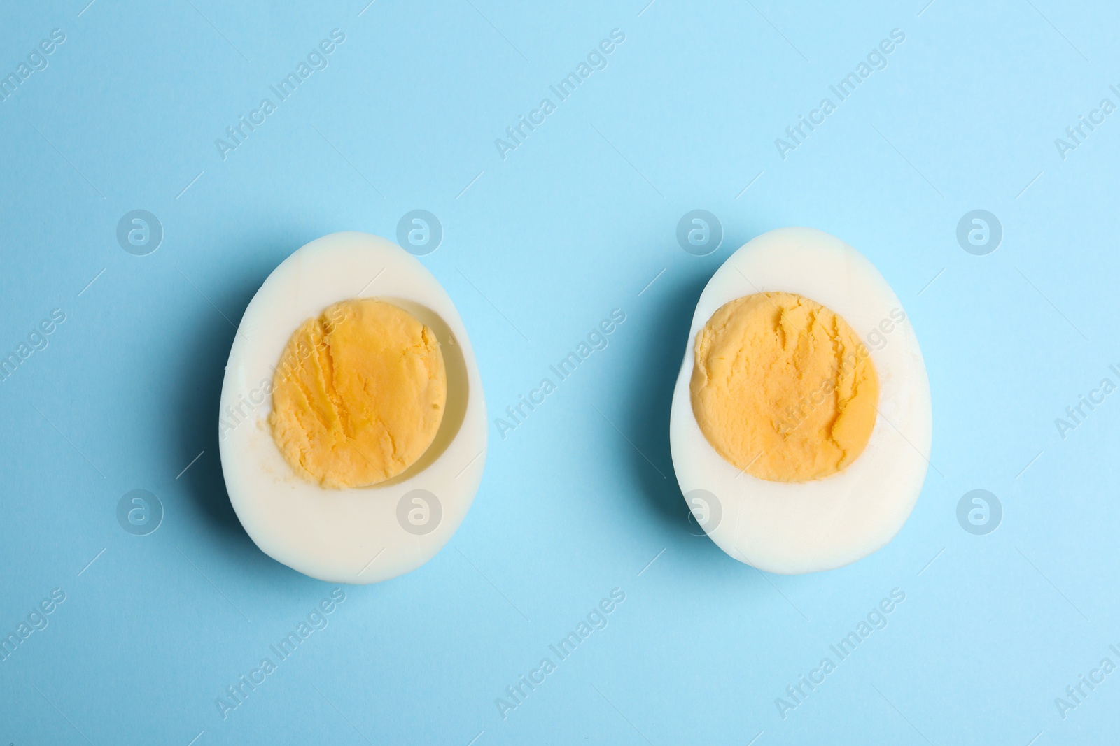 Photo of Halves of fresh hard boiled chicken egg on light blue background, flat lay