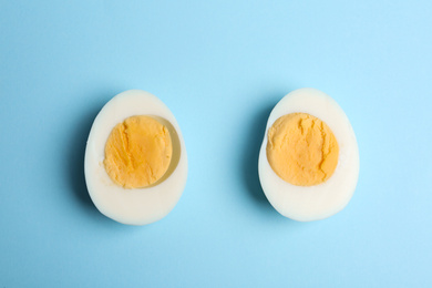 Photo of Halves of fresh hard boiled chicken egg on light blue background, flat lay
