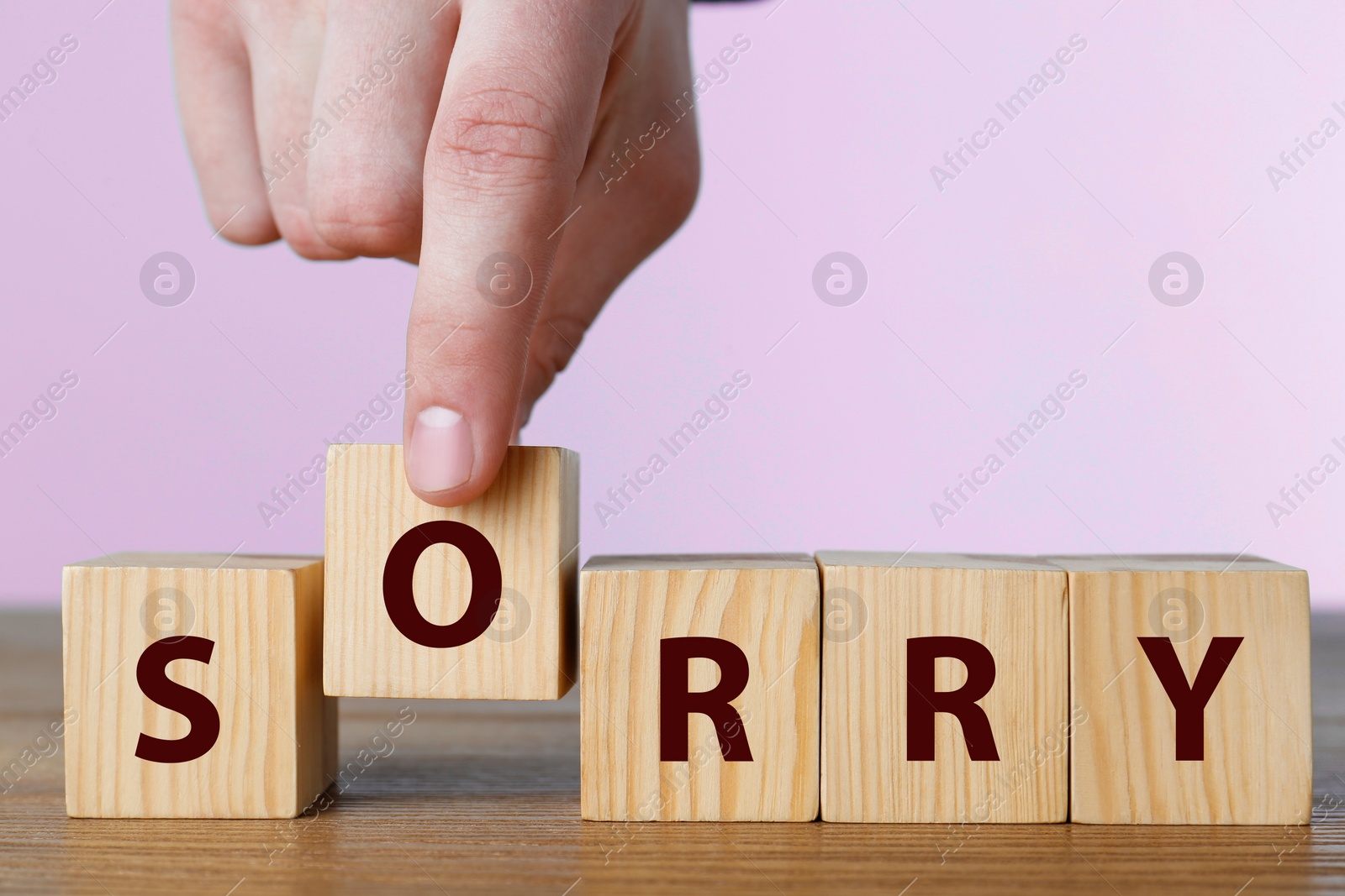 Image of Man putting cube with letter O to make word Sorry at wooden table, closeup