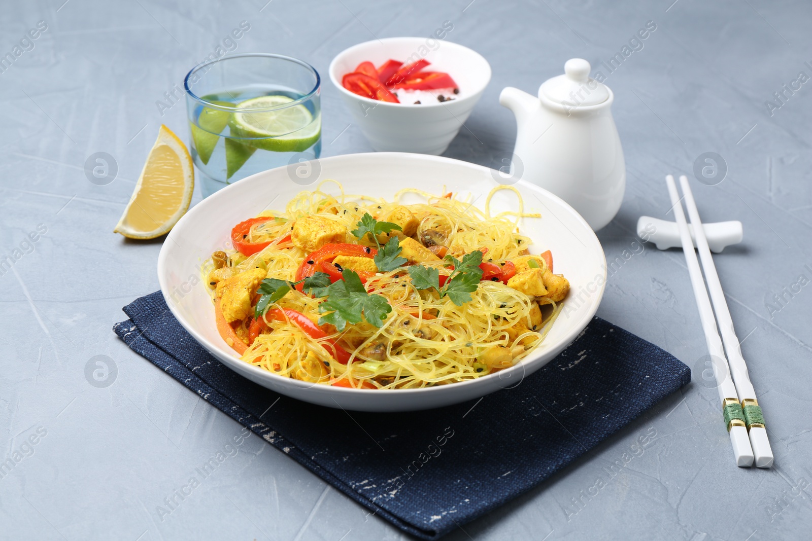 Photo of Stir-fry. Delicious cooked noodles with chicken and vegetables in bowl served on gray textured table