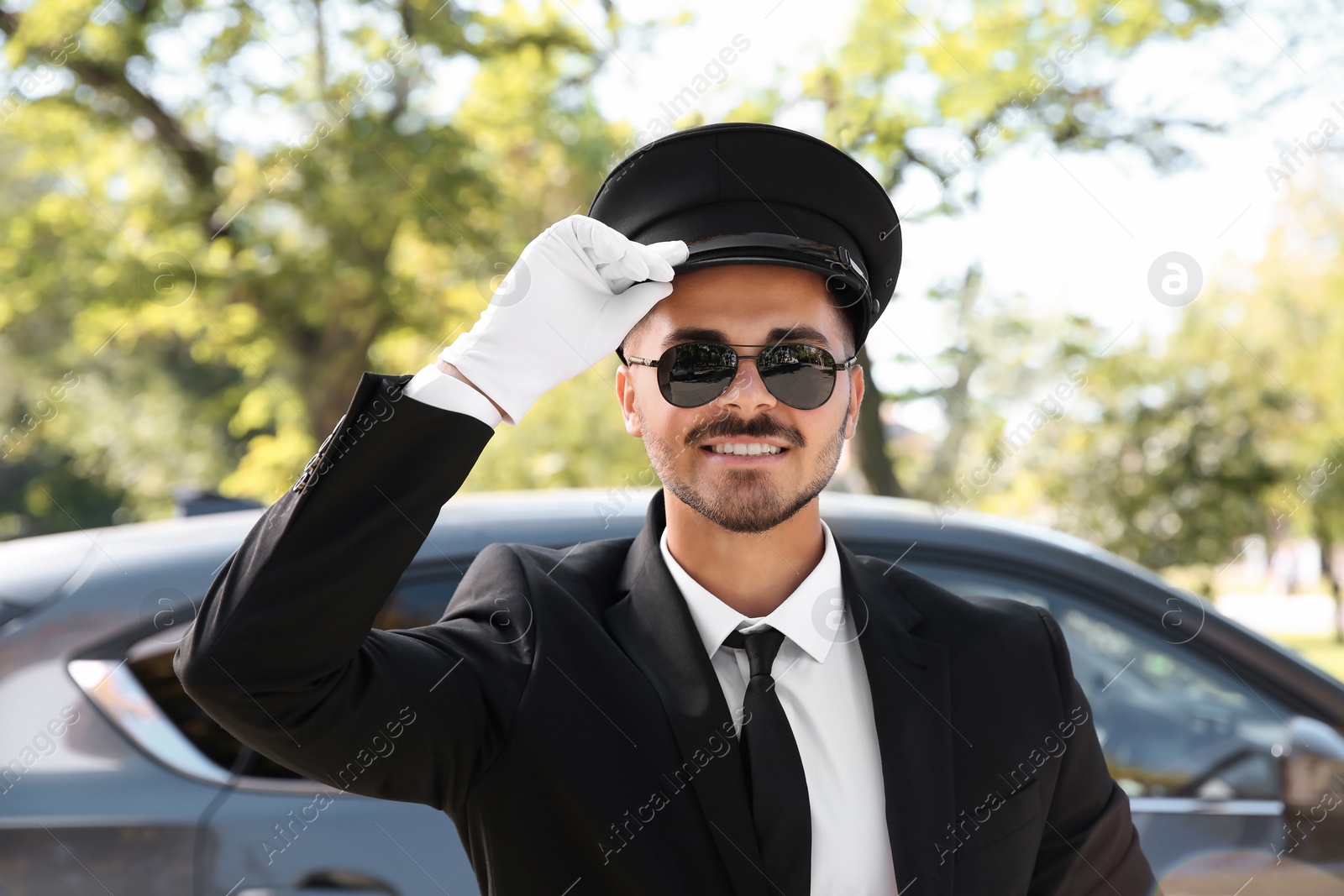 Photo of Young handsome driver standing near luxury car. Chauffeur service