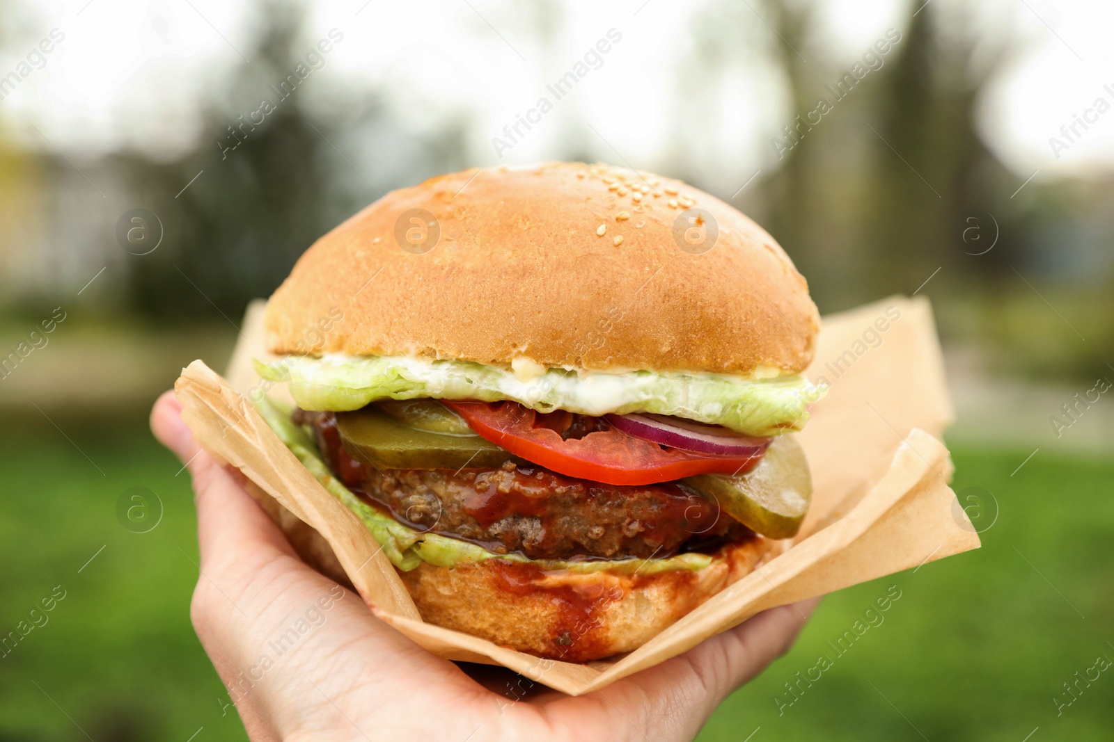 Photo of Little girl holding fresh delicious burger outdoors, closeup. Street food