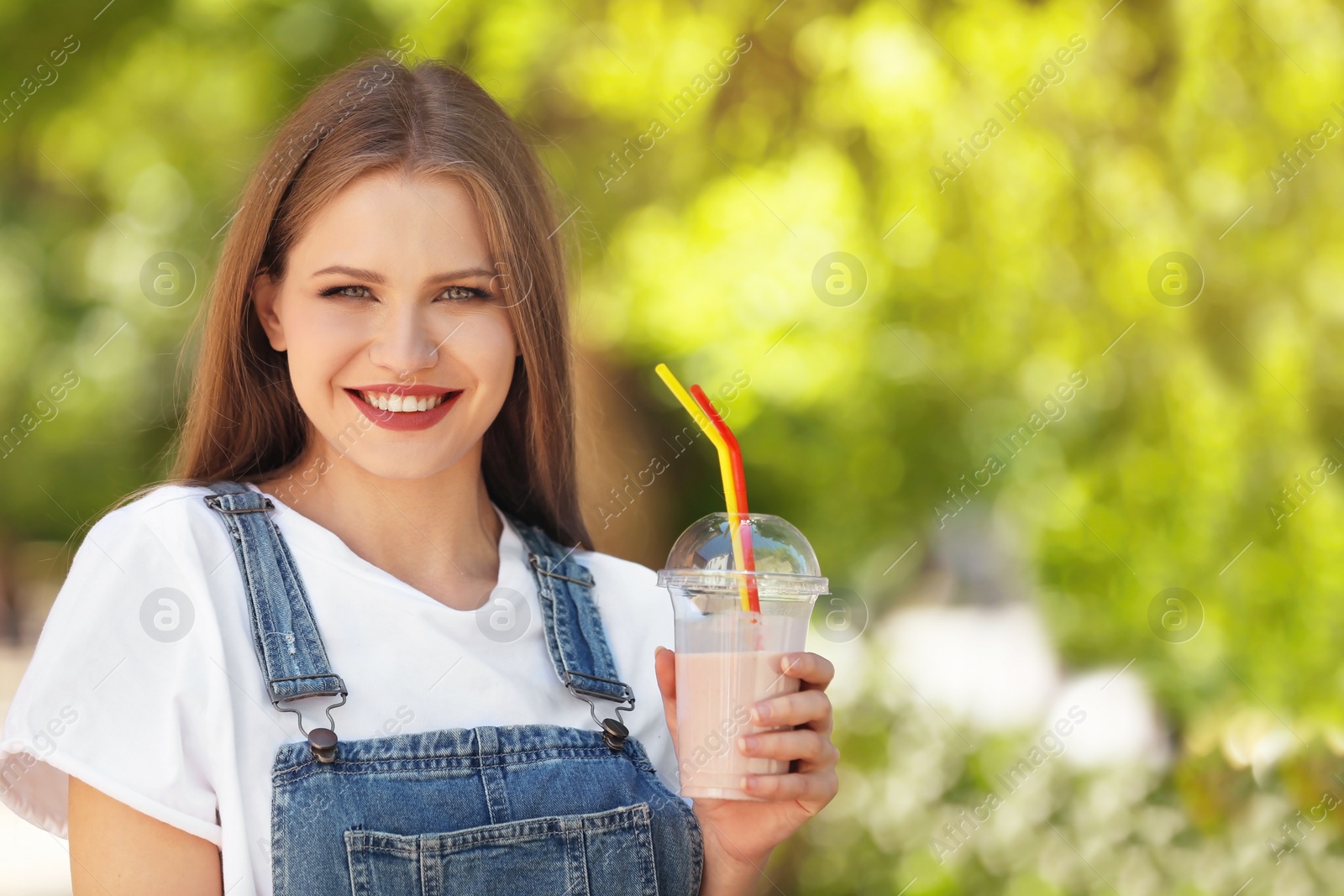 Photo of Young woman with cup of delicious milk shake outdoors