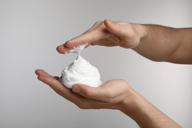 Man holding shaving foam on light grey background, closeup