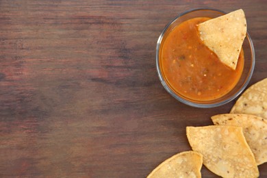 Photo of Tasty salsa sauce and Mexican nacho chips on wooden table, flat lay. Space for text