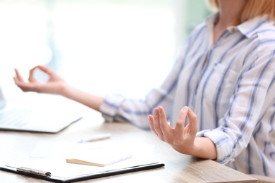 Photo of Beautiful woman meditating at table in office during break, closeup with space for text. Zen yoga