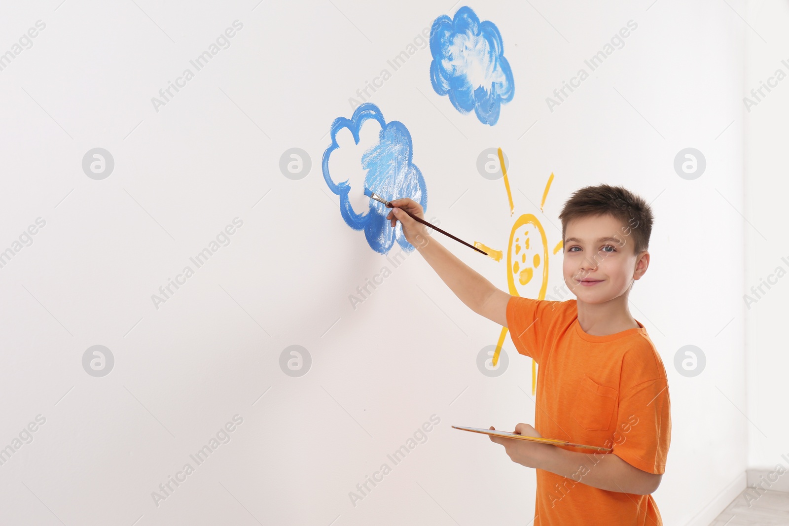 Photo of Little child painting cloud on white wall in room