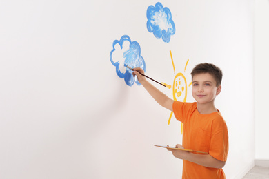 Little child painting cloud on white wall in room