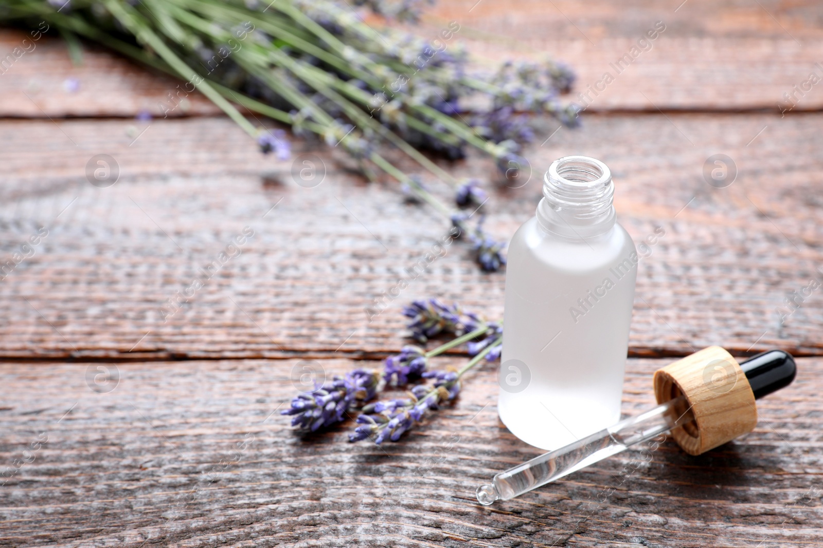 Photo of Bottle of lavender essential oil with flowers on wooden table, space for text