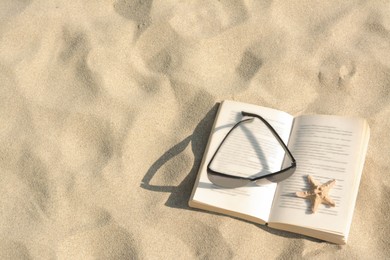 Photo of Beautiful sunglasses, book and starfish on sand, above view. Space for text