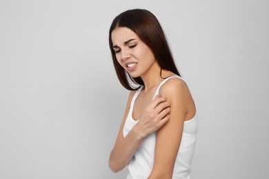 Photo of Young woman scratching shoulder on light background. Annoying itch