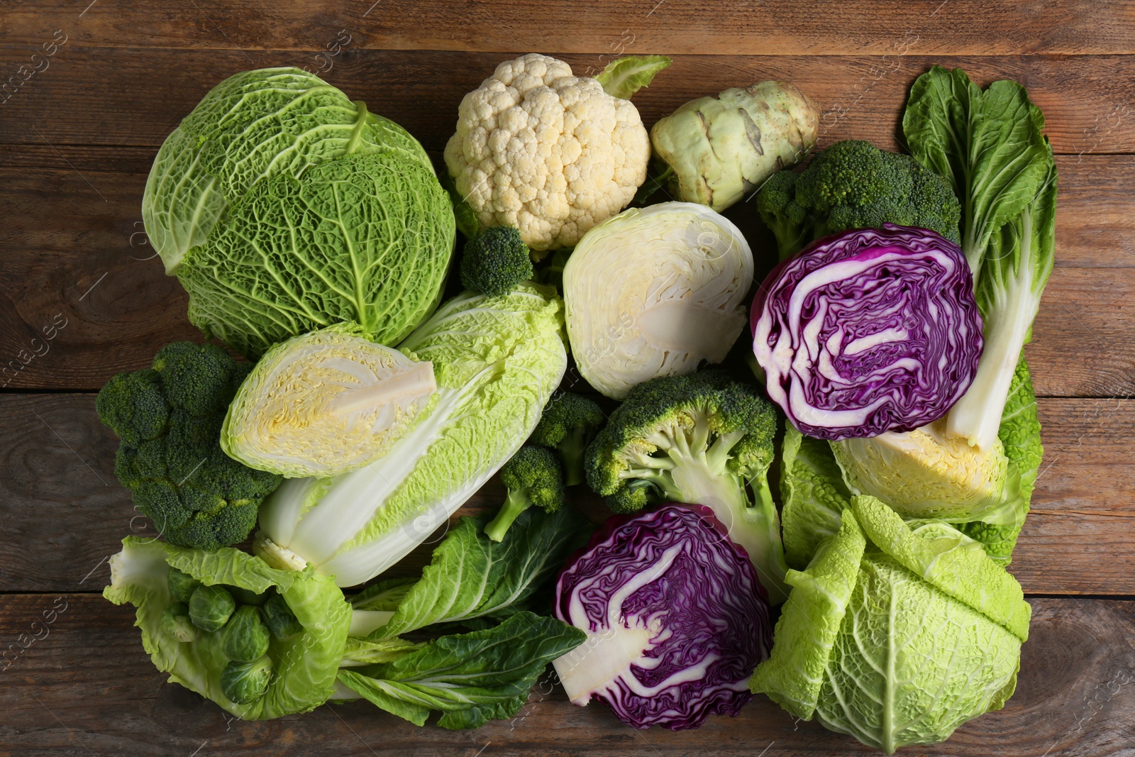 Photo of Different whole and cut types of cabbage on wooden table, flat lay