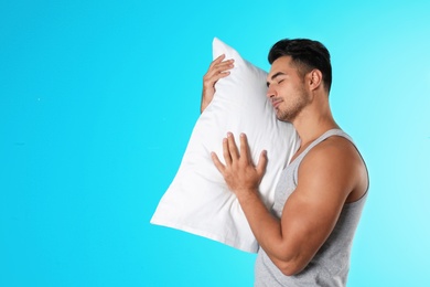 Young man with soft pillow on color background