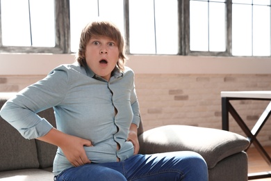 Emotional overweight boy sitting on sofa at home