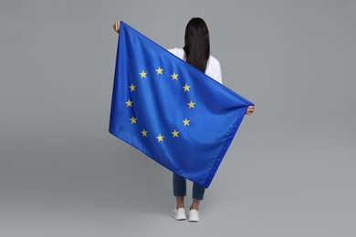 Photo of Woman holding European Union flag on light grey background, back view