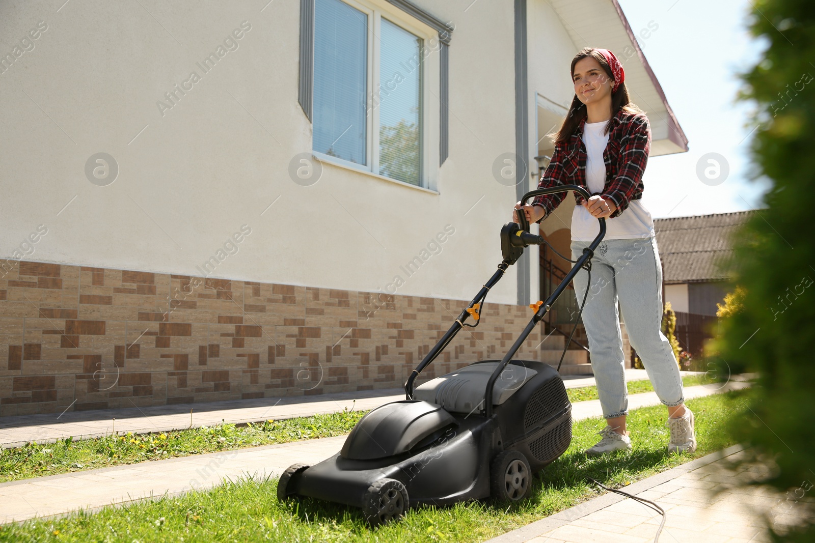 Photo of Woman cutting green grass with lawn mower on backyard