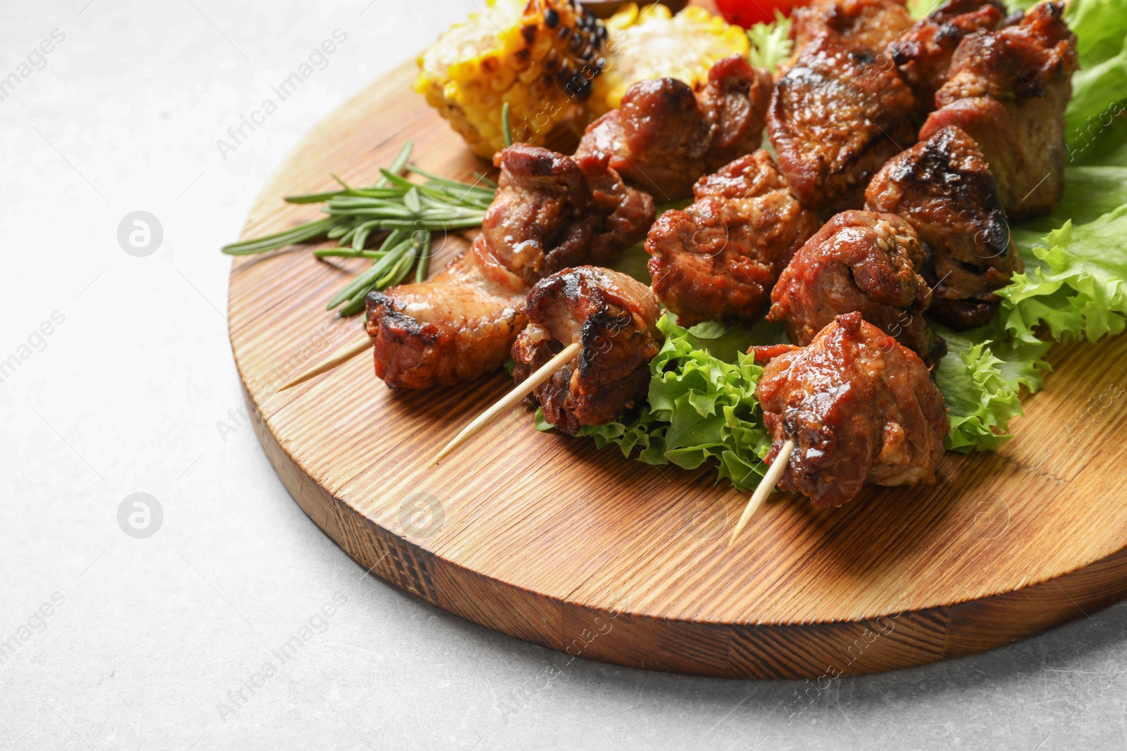 Photo of Wooden board with barbecued meat and garnish on grey background