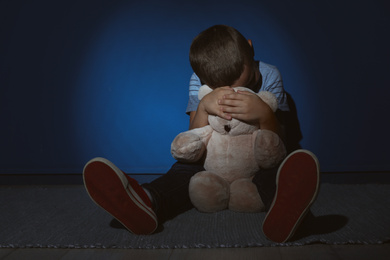 Sad little boy with teddy bear near blue wall. Domestic violence concept