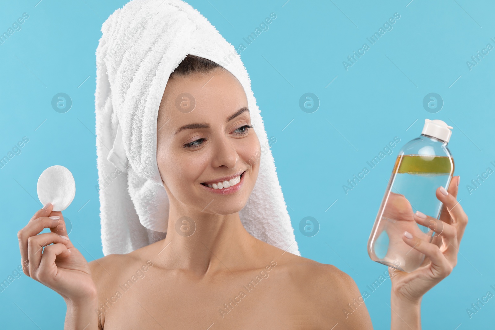 Photo of Removing makeup. Smiling woman with cotton pad and bottle on light blue background