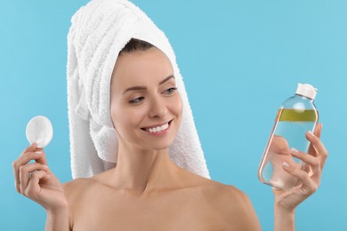 Removing makeup. Smiling woman with cotton pad and bottle on light blue background