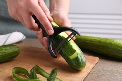 Photo of Woman peeling cucumber at wooden table indoors, closeup