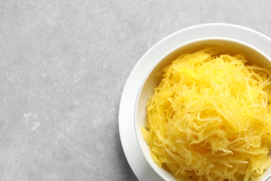 Photo of Bowl with cooked spaghetti squash on grey background, top view. Space for text