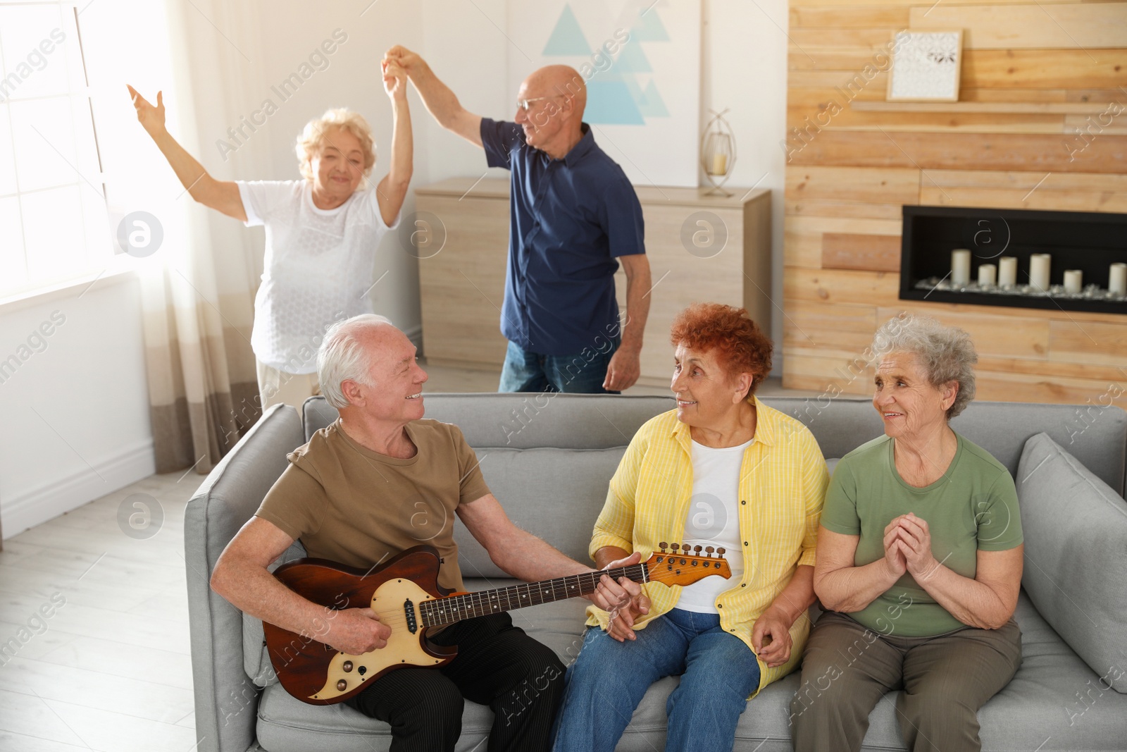 Photo of Elderly man playing guitar for his friends in living room