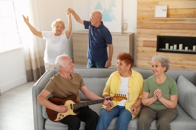 Photo of Elderly man playing guitar for his friends in living room