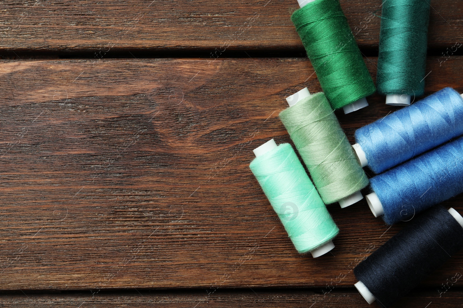 Photo of Different colorful sewing threads on wooden table, flat lay. Space for text