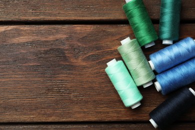 Photo of Different colorful sewing threads on wooden table, flat lay. Space for text