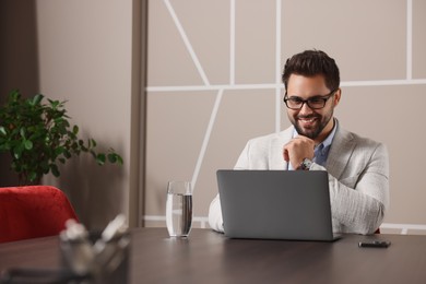 Photo of Happy young man with glasses working on laptop at table in office. Space for text