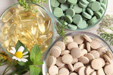Different pills, flowers and herbs on white table, flat lay. Dietary supplements
