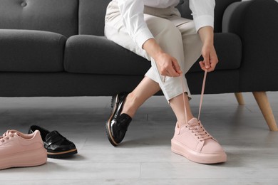 Photo of Woman taking off uncomfortable shoes and putting on sneakers in office, closeup