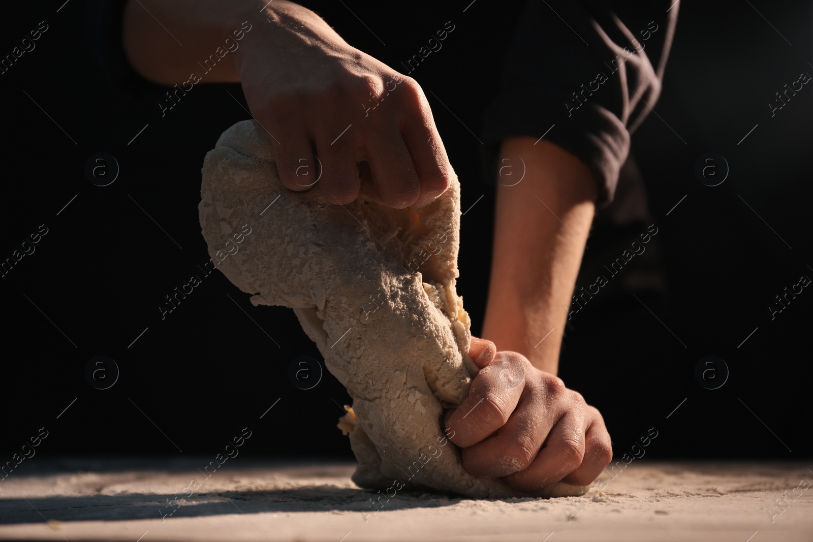 Photo of Making bread. Woman kneading dough at table on dark background, closeup