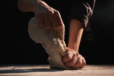 Making bread. Woman kneading dough at table on dark background, closeup