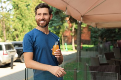Photo of Handsome man with bottle of delicious juice outdoors. Space for text