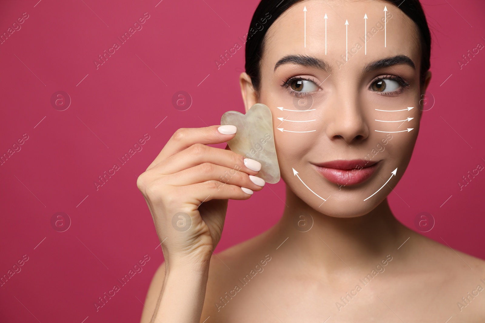 Image of Beautiful young woman doing facial massage with gua sha tool on crimson background, closeup