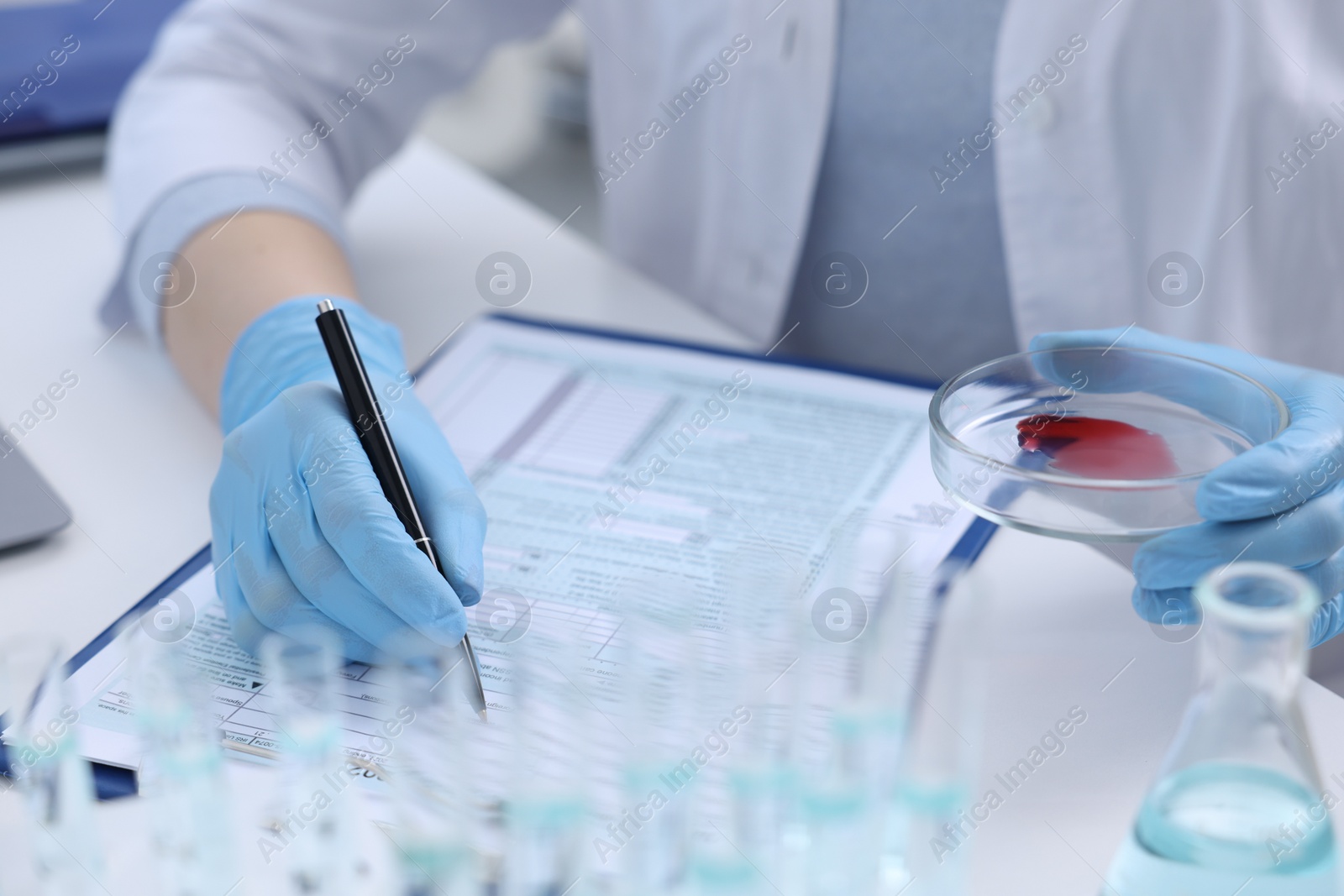 Photo of Laboratory worker holding petri dish with blood sample while working at white table, closeup